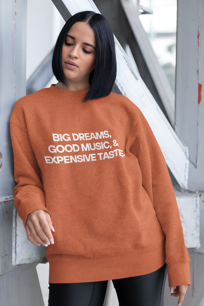 An Indian woman wearing a coral sweatshirt with "Big Dreams, Good Music, & Expensive Taste" written on it on a bridge