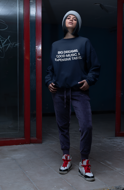 An Indian woman wearing a cool navy blue sweatshirt with "Big Dreams, Good Music, & Expensive Taste" written on it.