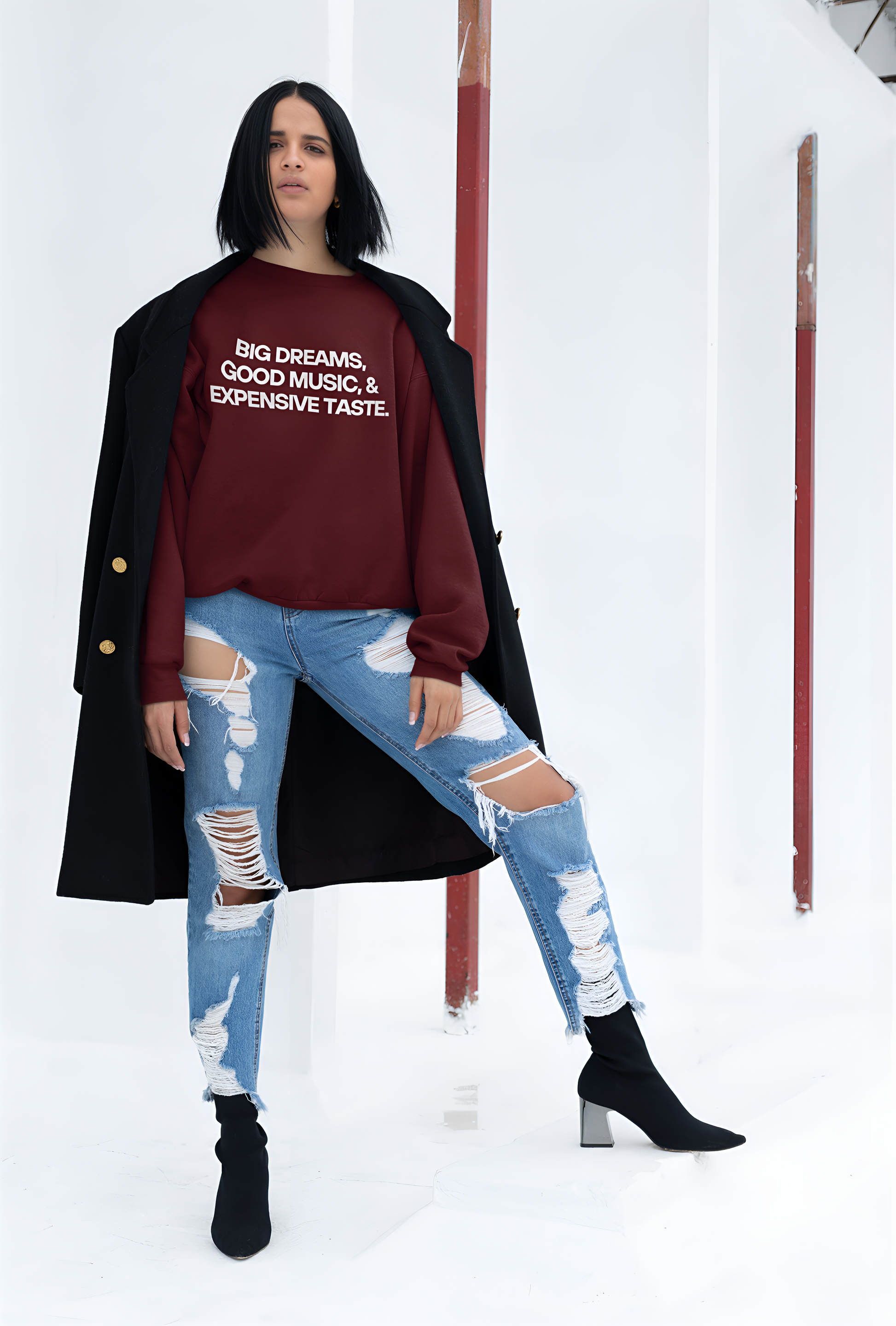 An Indian woman in heels wearing a maroon sweatshirt with "Big Dreams, Good Music, & Expensive Taste" written on it.  