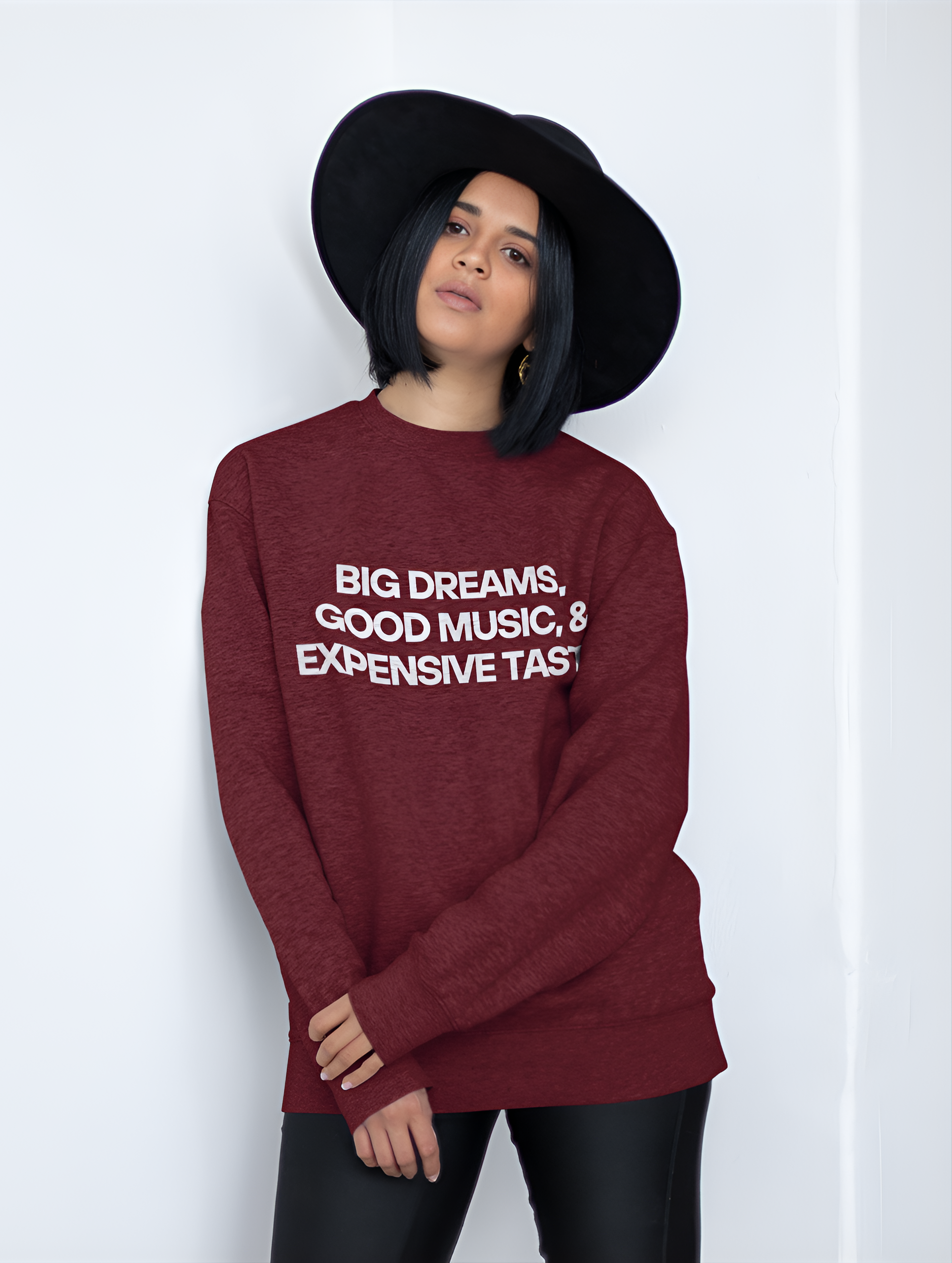 An Indian woman wearing a maroon sweatshirt with "Big Dreams, Good Music, & Expensive Taste" written on it in a hat and shorts